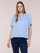 Blusa celeste de lyocell ultraliviano, de estilo romántico y silueta holgada. Presenta escote redondo con abertura en V y botones frontales, canesú fruncido y mangas cortas amplias.