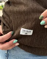 Buzo de punto texturizado en color marrón, de corte clásico con cuello redondo, mangas largas y puños y cintura elastizados. Incluye una pequeña etiqueta blanca con la marca en el borde inferior.