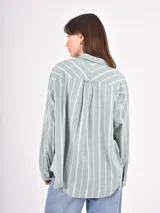 Camisa de corte holgado con estampado de rayas verticales en tonos verde y blanco, cuello clásico, cierre frontal con botones y bolsillo en el pecho.