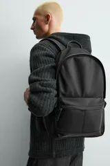Mochila de tejido técnico en color negro, con compartimento principal con cierre de cremallera, bolsillo frontal con cierre y compartimento interior acolchado para dispositivos electrónicos. Cuenta con parte posterior acolchada, banda de sujeción para equipaje, asa de mano superior y correas de hombro ajustables.