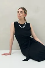 Vestido largo de punto color negro, sin mangas, con diseño entallado y un lazo lateral que permite ajustar la cintura.