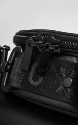 Bolso circular de estructura rígida, color negro, diseñado para el transporte de auriculares y accesorios. Cuenta con manija superior reforzada, correa de hombro ajustable con logo grabado, cierre perimetral y bolsillo trasero de acceso rápido.