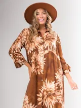 Vestido camisero largo color marrón con estampado de flores blancas, con cuello camisero, abotonado al frente y mangas largas con puños abotonados.