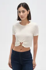 Top de manga corta con textura arrugada, cuello redondo y diseño corto. Presenta un detalle de frunce central con una argolla metálica y un botón decorativo en el ruedo.