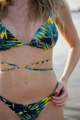 Conjunto de bikini con estampado de hojas de palmera en tonos verde, amarillo y negro. El corpiño es de triángulo con tirantes finos y la bombacha es colaless con tirantes ajustables.