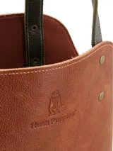 Matera de cuero con diseño bicolor en tonos marrón y verde oliva, con correas largas para hombro y detalles de remaches metálicos. Incluye logo de la marca grabado en el frente.