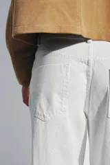 Jeans de tiro medio y corte barrel leg, color blanco roto. Presenta cinco bolsillos y cierre frontal con cremallera, botón y gancho metálico.