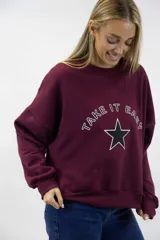 Buzo bordó con cuello redondo, mangas largas y puños y ruedo elastizados. Cuenta con estampa frontal que dice "Take It Easy" junto a un diseño de estrella negra delineada en blanco.