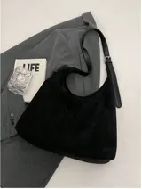 Bolso tipo hobo de material tipo gamuza o nobuk, color marrón camel. Presenta un diseño de silueta suave y caída, con una correa de hombro delgada de cuero liso del mismo tono.