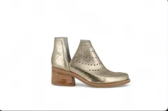 Botín de cuero blanco con textura de crocco y charol, diseño con calados circulares y aberturas laterales en forma de V. Cuenta con taco foliado de madera y vira cosida.