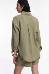 Camisa de manga larga color verde militar en tejido de gasa de algodón, con cuello camisero, cierre frontal de botones y dos bolsillos plaqué con solapa en el pecho.