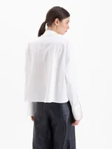 Camisa de poplín de algodón con corte holgado y largo hasta la cadera. Presenta cuello clásico con detalle de herraje metálico, cartera oculta con botones al tono y puños anchos con botones.
