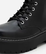 Bota tipo coturno de caña media, confeccionada en poliuretano color negro, con cierre frontal de cordones, cremallera lateral y suela track robusta.