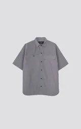 Camisa de manga corta de poplin, color gris, con silueta oversize. Presenta dos bolsillos delanteros, uno con solapa y otro con ojal y botón.