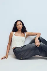Top estilo corset de color blanco con escote cuadrado y tirantes anchos. Presenta paneles laterales y centrales con tejido drapeado, estructura entallada y cierre posterior con cremallera.