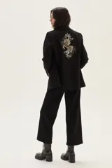 Blazer negro de corte clásico con cierre frontal de botones y detalle de bordado artístico en la espalda que representa un caballo y motivos florales.