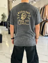Remera oversize color negro con efecto gastado (acid wash), manga corta, y gran estampado en la espalda de una calavera con la inscripción "Mushkana Born to Chill".