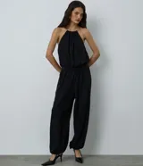 Mono largo de color negro, confeccionado en microfibra, con diseño de frente única y detalle de adorno metálico tipo collar en el escote. Presenta una silueta holgada con cintura elástica y botamangas ajustadas.