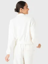 Buzo estilo polerón color blanco off-white, confeccionado en tela suave y ligera. Presenta cuello alto, cierre frontal con tapeta de botones a presión, bolsillos frontales con solapa y pretina elástica en la cintura.