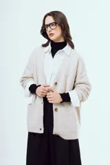 Cardigan de punto color beige, con escote en V, cierre frontal de botones carey, mangas largas y bolsillos frontales aplicados.