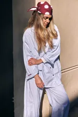 Pijama de dos piezas de algodón a rayas celestes y blancas, compuesto por una camisa de manga larga con botones y ribetes marrones, y un pantalón largo de corte recto con elástico en la cintura.