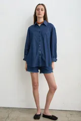 Camisa de jean azul, de corte holgado y manga larga, con cuello camisero y cierre frontal de botones oscuros.
