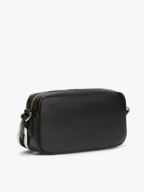 Cartera tipo bandolera Tommy Hilfiger de color negro, con acabado liso, diseño compacto y esquinas redondeadas. Cuenta con cierre de cremallera superior, inscripción y logotipo de la marca en bajo relieve dorado en el frente, y una correa cruzada ancha ajustable de jacquard a rayas en blanco y negro con la marca escrita.