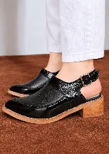 Zapatos destalonados de cuero negro con textura grabada y acabado charol, diseño de inspiración artesanal, taco bajo de aspecto madera y pulsera ajustable con hebilla metálica.