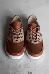 Sneakers de cuero marrón con detalles en cobre, paneles texturizados, talón plateado y suela blanca.