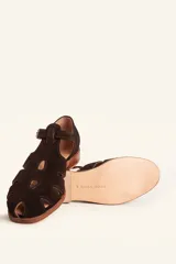 Sandalias de gamuza color marrón, estilo romano con diseño en T, tiras con aberturas laterales y cierre de hebilla metálica en el tobillo. Cuenta con tacón bajo de madera.