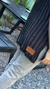 Chaleco tejido de punto acanalado vertical en color negro con hilos de lurex plateados. Presenta cuello redondo, hombros amplios con efecto de hombrera caída y tajos laterales en el ruedo.