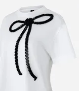 Remera blanca de algodón con cuello redondo, mangas cortas y bordado de lazo negro en la parte delantera.