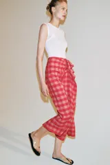 Falda midi de tiro medio, con estampado a cuadros vichy en tonos rojo y rosado, detalle de volantes en el delantero y cierre lateral con cremallera oculta.
