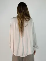 Camisa de satén color naranja óxido, con cuello mao y lazo para anudar. Presenta volados decorativos en el frente y en las mangas, las cuales son largas y terminan en puños abotonados.