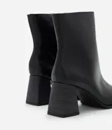 Bota de caña baja en cuero sintético color negro, con punta cuadrada y taco bloque de altura media con textura amaderada.