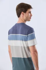 Remera de manga corta y cuello redondo, con diseño de bloques de color y franjas horizontales en tonos azul, celeste y gris, con pequeño logo bordado en el pecho.