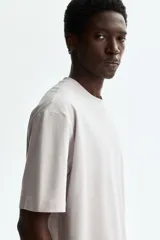 Remera boxy de punto de algodón pesado, color gris claro, con cuello redondo ribeteado acanalado, hombros caídos y mangas cortas de corte holgado.
