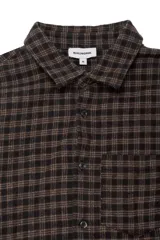 Camisa de manga larga confeccionada en franela con estampado a cuadros en tonos oscuros. Presenta cuello clásico, cierre frontal con botones, puños abotonados y un bolsillo aplicado en el pecho.