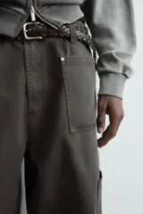 Pantalón de corte relaxed fit confeccionado en algodón, color gris oscuro. Presenta bolsillos delanteros, bolsillos laterales tipo cargo en las perneras y cierre frontal con cremallera y botón.