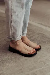Sandalia de cuero color tostado con tiras anchas, tira en el talón y hebilla metálica rectangular ajustable. Cuenta con suela de goma con tacón bajo y plataforma.