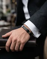 Pulsera masculina con banda central de cuerina negra grabada con diseño de guarda griega y detalles laterales en acero inoxidable.