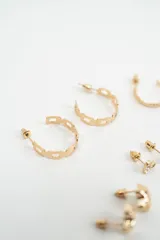 Set de caravanas compuesto por múltiples pares de aros en tono dorado, incluyendo aros tipo argolla de diferentes tamaños, aros con perlas pequeñas, aros con formas geométricas y aros con cristales engarzados.