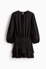 Vestido corto negro de mezcla de viscosa, con escote redondo, abertura frontal con tiras finas y mangas largas abullonadas con puños elásticos. Presenta sección entallada en la cadera con alforzas y falda corta con volados escalonados.