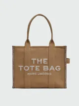 Cartera tipo tote bag Marc Jacobs modelo The Large Tote, color marrón con el texto "THE TOTE BAG MARC JACOBS" impreso en blanco en el frente. Confeccionada en lona resistente, cuenta con asas superiores dobles para llevar al hombro o en la mano.