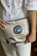 Sobre de mano color bordó en cuero charolado, con solapa frontal decorada con una piedra ágata natural engarzada. Incluye correa larga extraíble y cierre trasero.