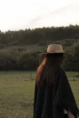 Ruana tejida en telar con lana merino, color negro con sutiles destellos brillantes. Presenta un diseño abierto con flecos en el ruedo.
