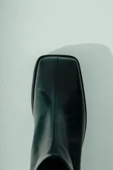 Bota de caña media confeccionada en cuero negro, con diseño minimalista, punta cuadrada y taco ancho geométrico.