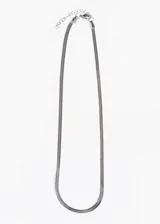 Cadena plateada de acero quirúrgico con eslabones planos tipo serpiente, cierre de mosquetón y cadena de extensión.