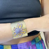 Brazalete rígido dorado con textura martelé y aplique de pulpo turquesa con incrustaciones de circonitas.