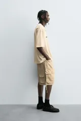 Camiseta de algodón de corte relajado, color beige claro, con cuello redondo y manga corta. Presenta un estampado central de garabatos negros con texto en mayúsculas que dice "TAKE RIGHT STEP FIND A RIGHT CORD".